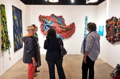 Four people stand in front of a number of fabric works in a booth.