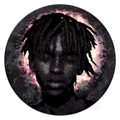 A circular image of young black man's face with braided heir set against a dark background with a bloom of orange-red white light behind him.