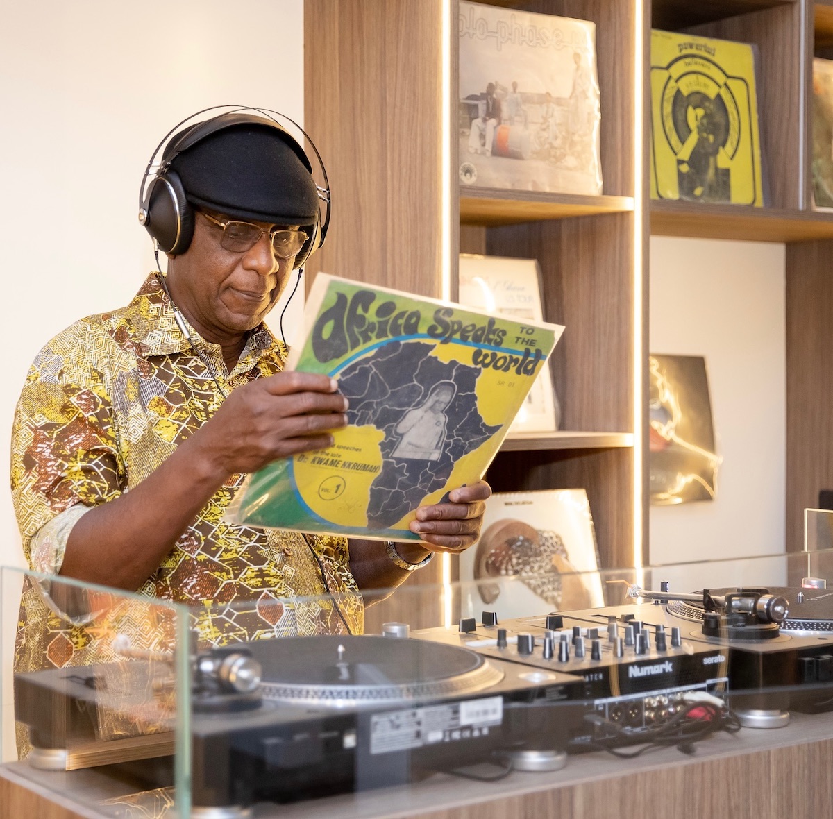 A Black man with headphones holding a vinyl album over a turntable.