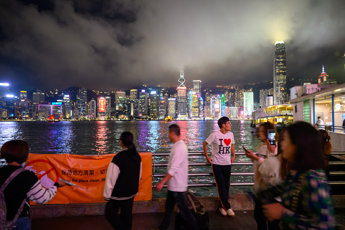 HONG KONG, CHINA - FEBRUARY 21: A tourist wearing an 'I love HK' shirt poses with a view of the Hong Kong skyline in the background as seen from Kowloon on February 21, 2024 in Hong Kong, China. Tourism levels returned to pre-pandemic numbers for the first time as Hong Kong celebrates the first Lunar New Year without pandemic restrictions this month. (Photo by Alexi Rosenfeld/Getty Images)