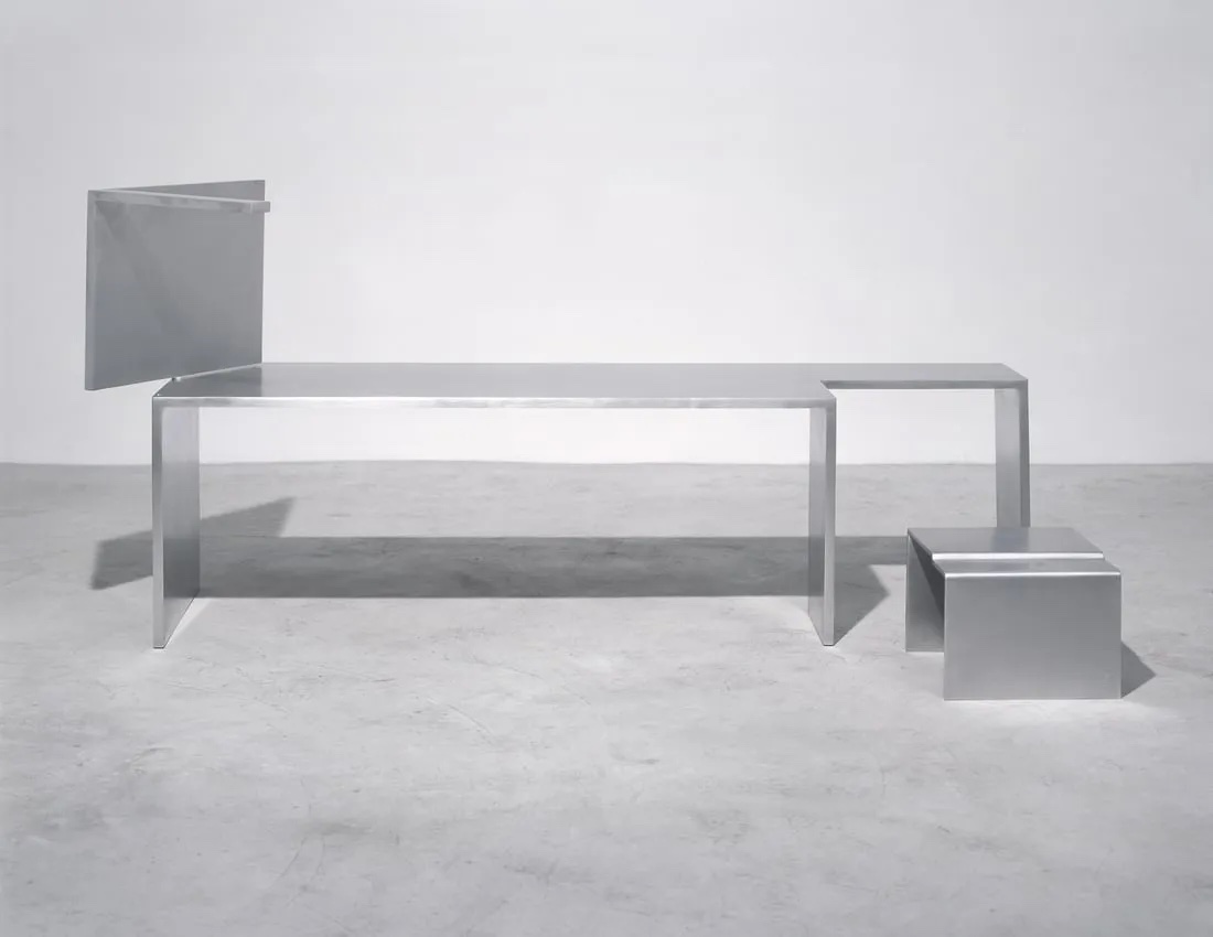 A aluminum bench in an empty, grey room.